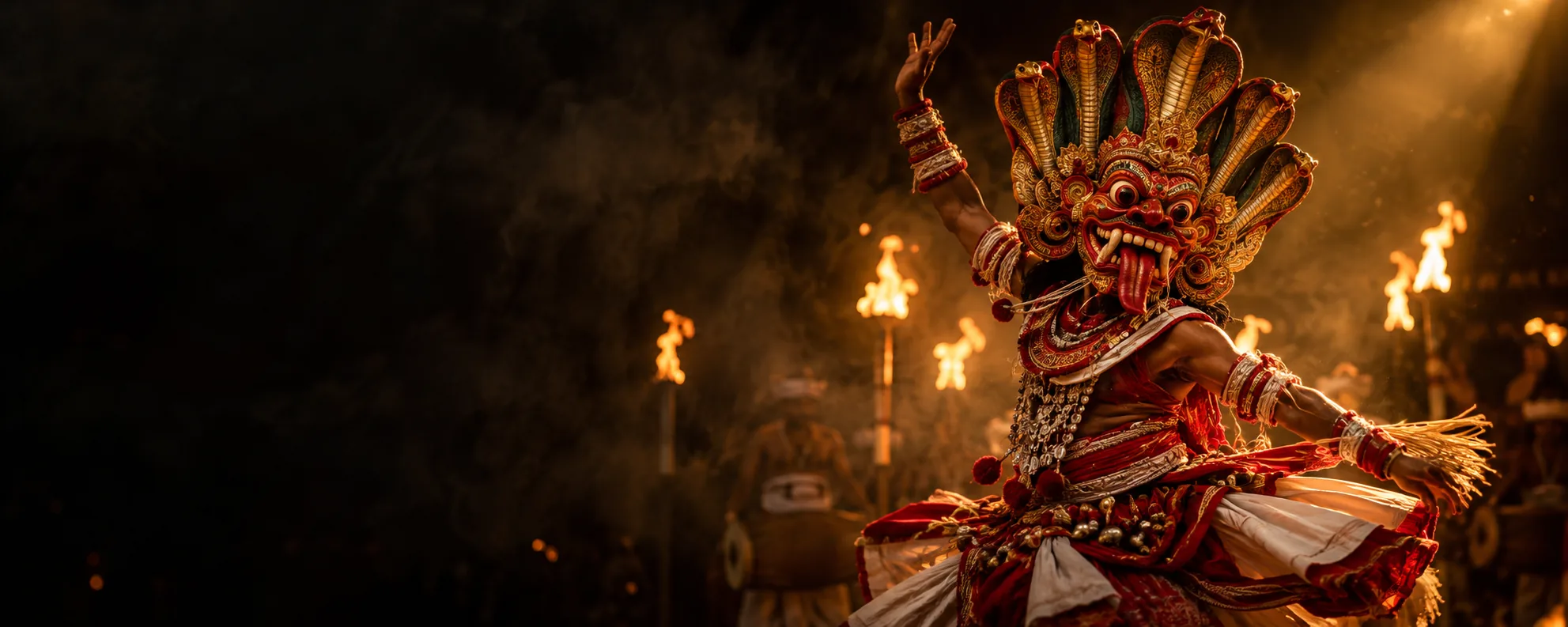 A masked dancer in a Naga raksha mask crowned with cobra hoods, torches burning behind